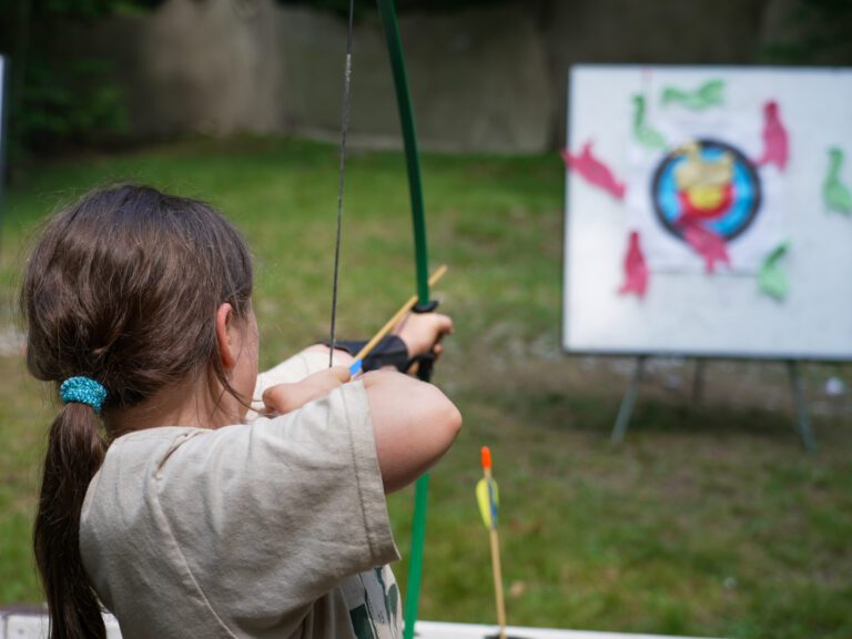 A young girl aims a bow at an archery target