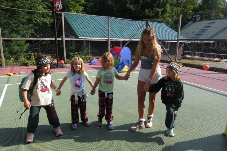 A camp counsellor on a tennis court looks after five children