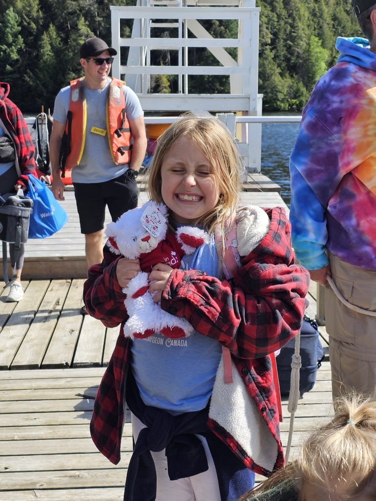 A child scrunches their face up with joy while squeezing a stuffie on a wooden dock