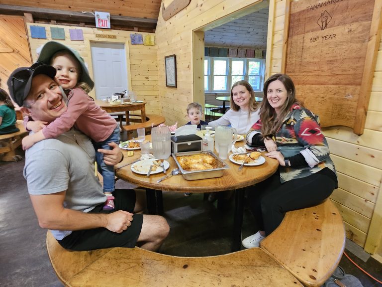 A family of five sit around a table in a wood-panelled dining hall