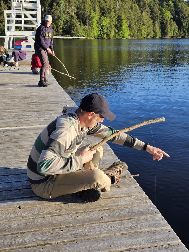A person sitting on a dock leans forward to adjust their line