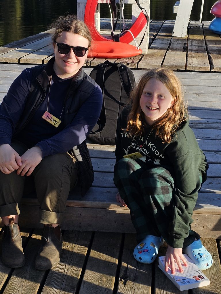 Two smiling people sit on a dock