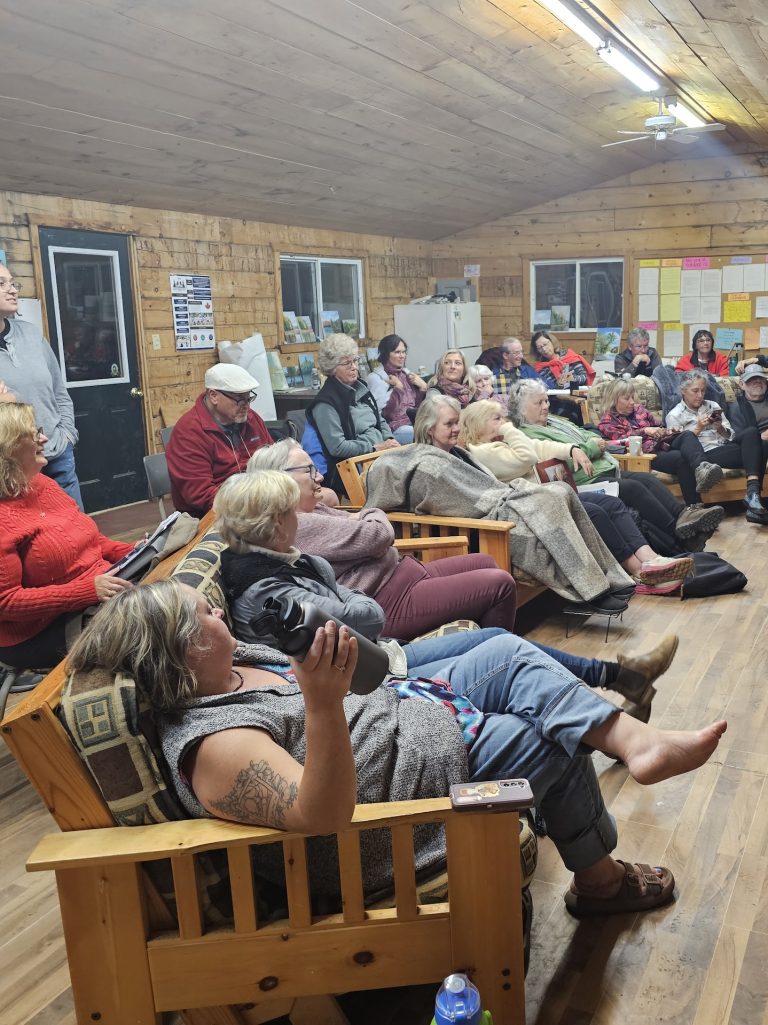 A large group of people sit in a wood-panelled gathering space at night