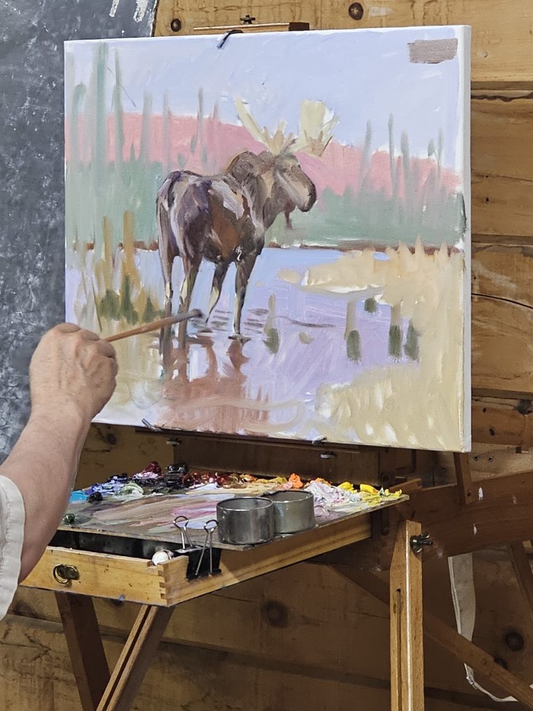 A hand works on a painting of a moose
