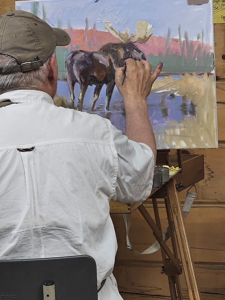 A man touches up a painting of a moose