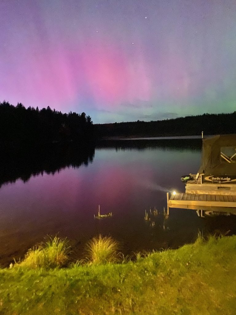 Pinkish-purple green northern lights over a quiet lake