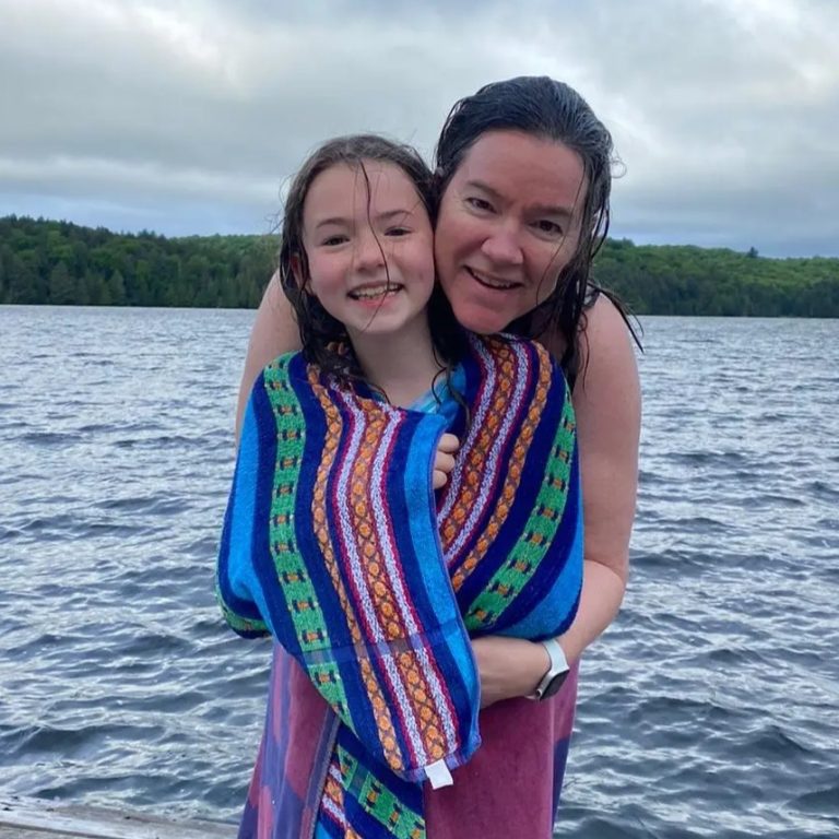 A woman wraps a child in a bathing suit in a towel and pauses for a hug