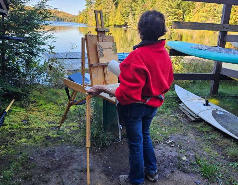 A person stands in front of an art easel beside a rack of kayaks