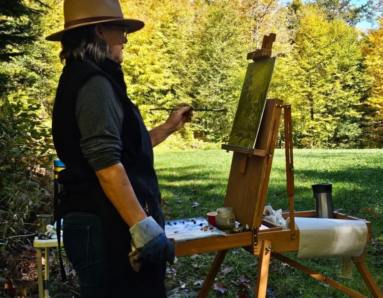 A painter reaches with their brush to add to a landscape painting