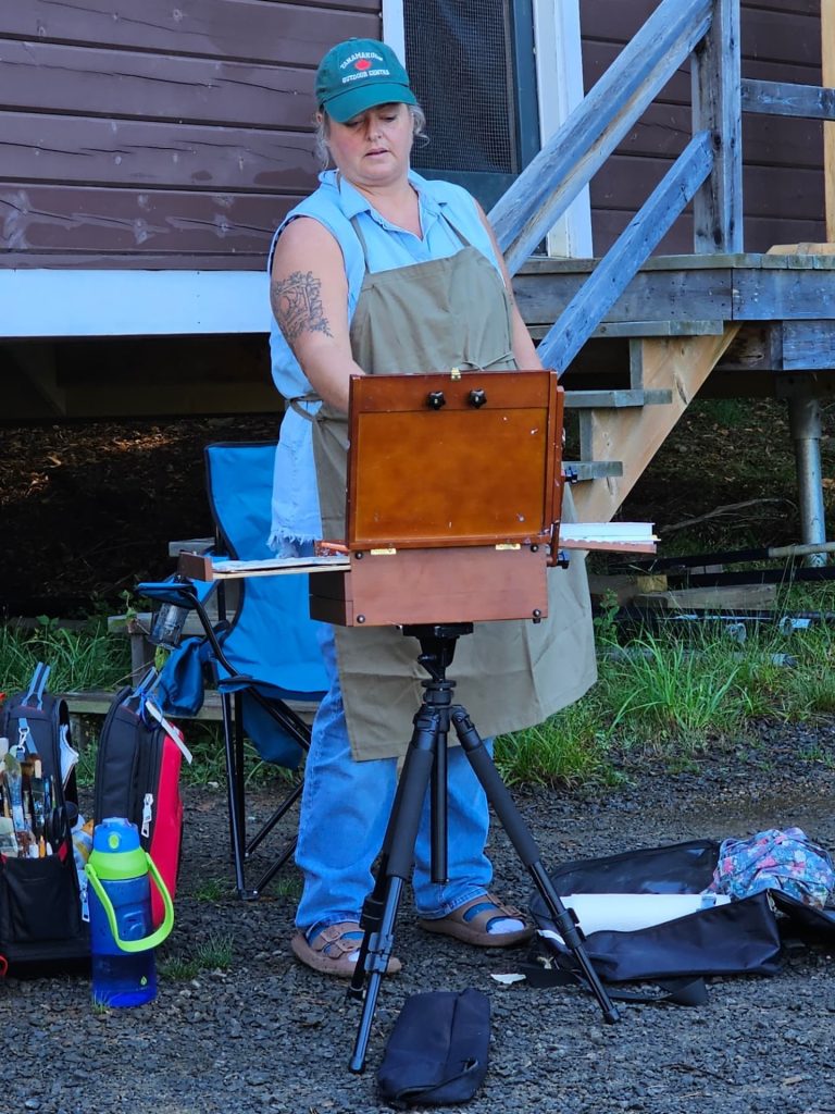 A woman works on painting, her easel turned away from the camera