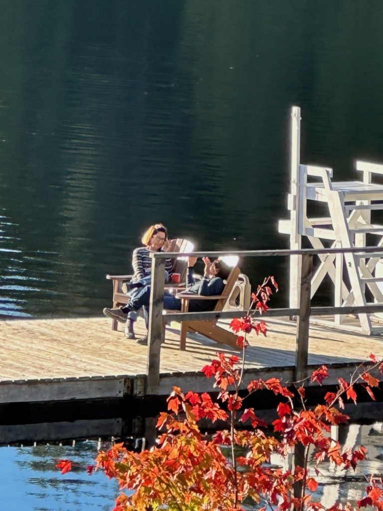 Two people in Muskoka chairs on a dock, seen from afar