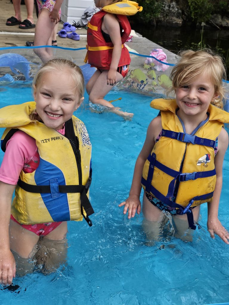 Two kids in lifejackets stand in a pool smiling
