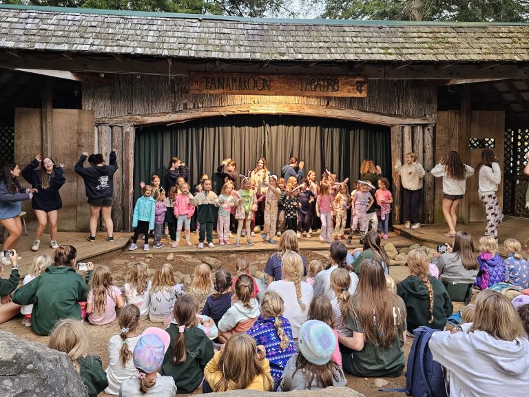 An outdoor performance, with a large group of kids performing and a large young audience