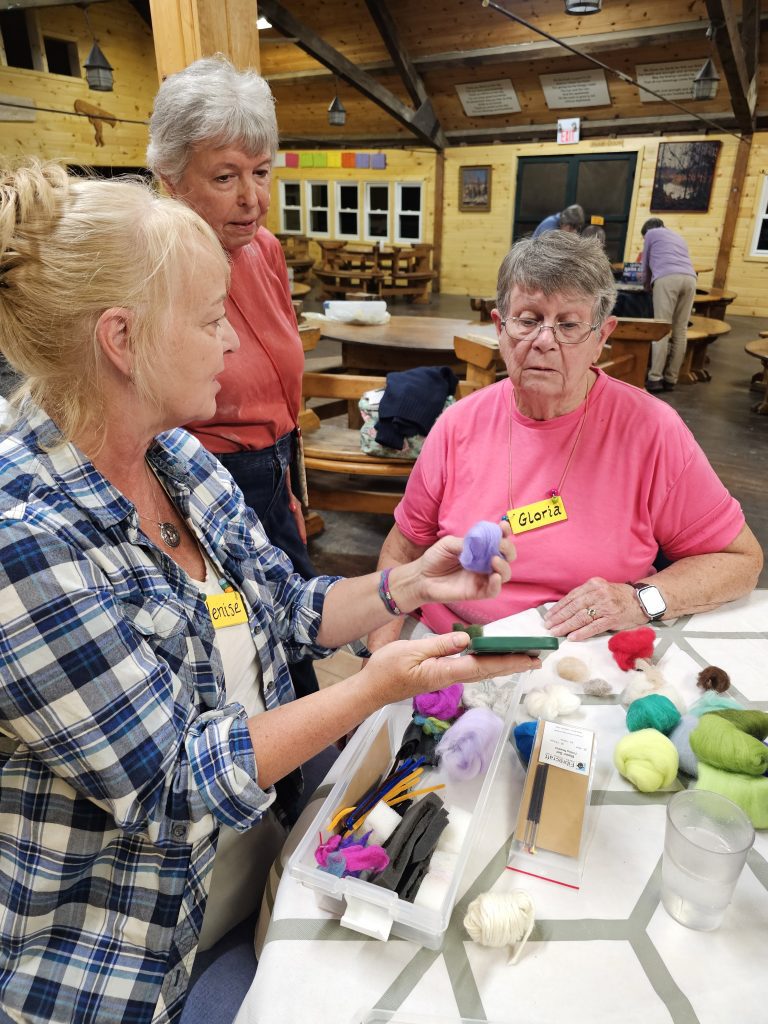 A woman shows a selection of skeins of yarn to two other women