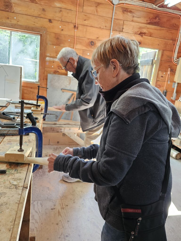 A person does some kind of woodworking with a piece of wood clamped to the table