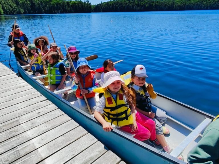 A large canoe beside a dock, full of children in life jackets
