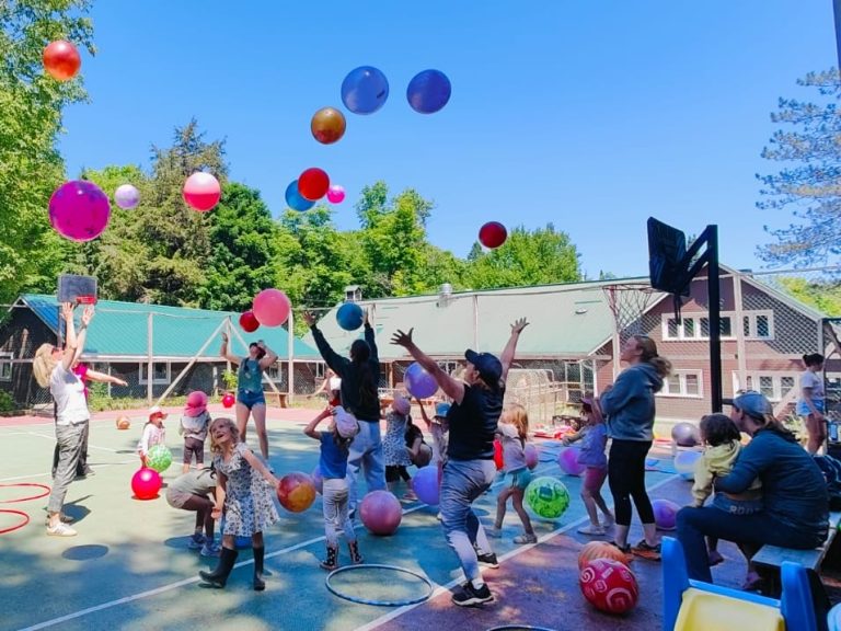 Kids and adults play a game involving multiple balloons on a tennis court