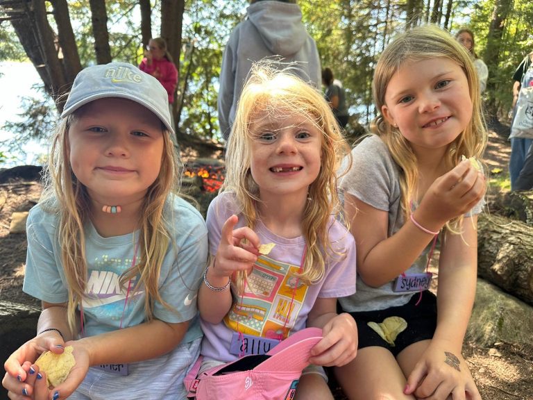 Three smiling kids sitting outdoors pose for a photo