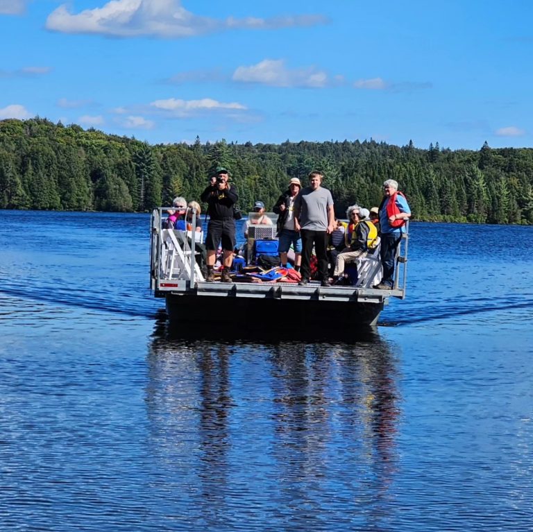A pontoon boat in the middle of a lake with a large group on it