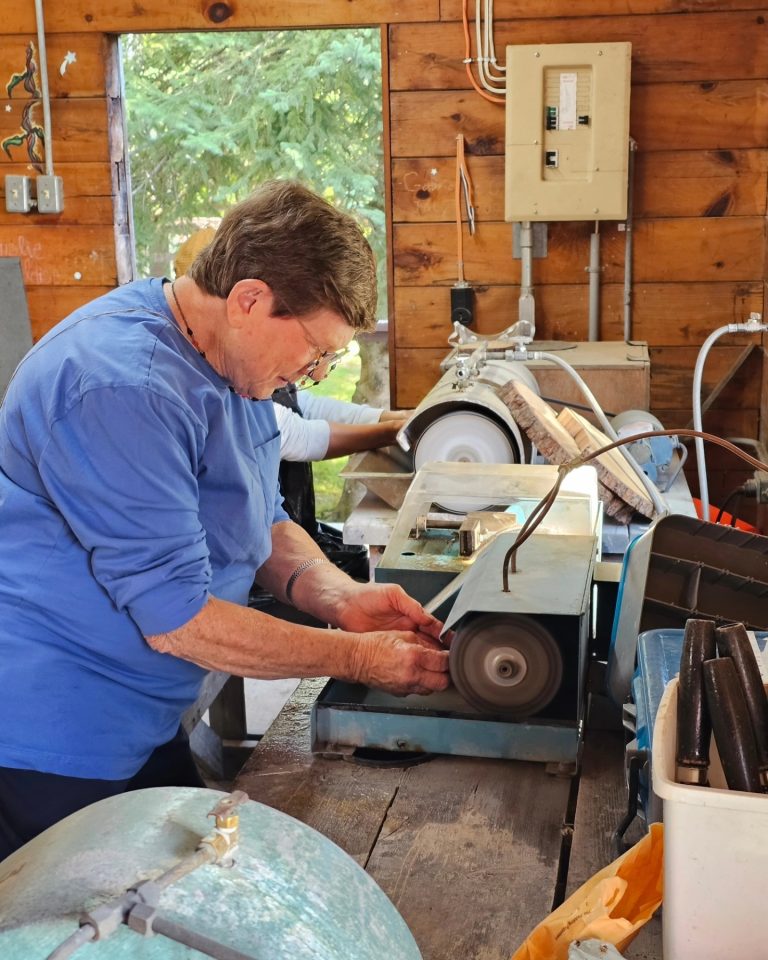 A person in a workshop, door open behind them, holds something against an electric sander