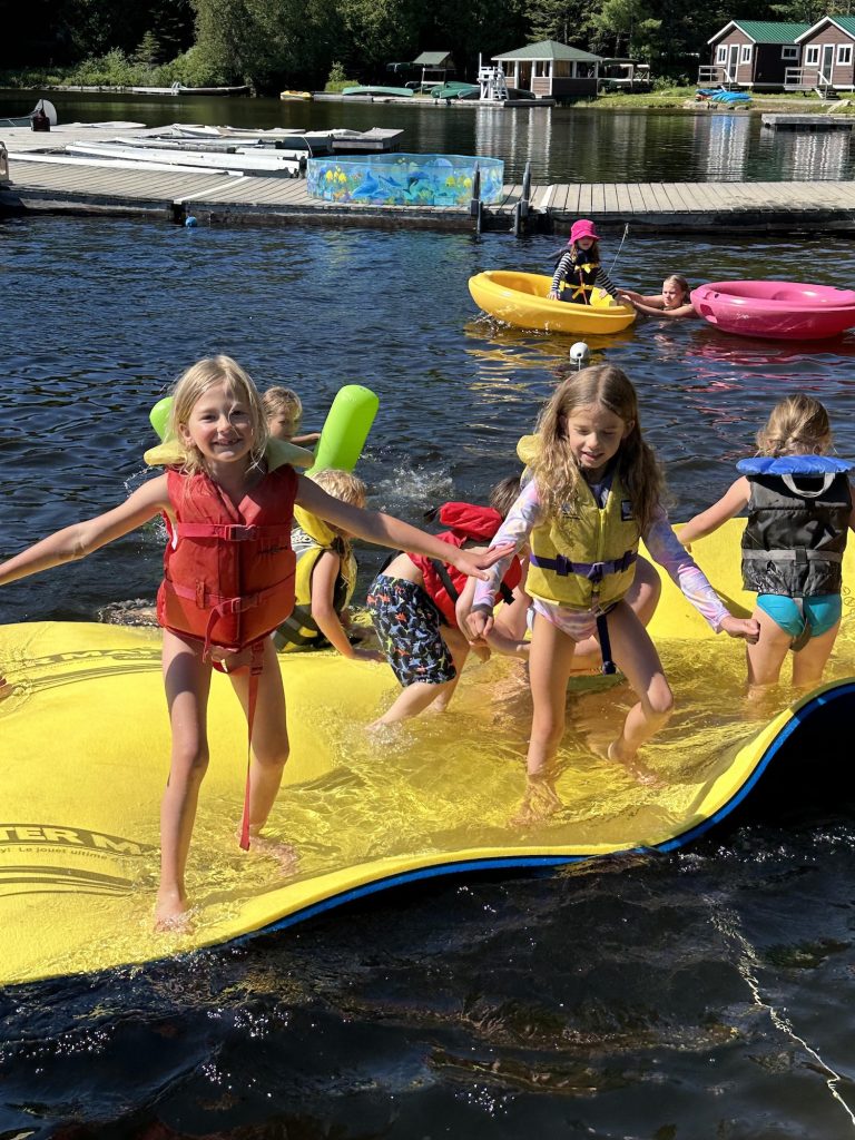 Children leap from a floating yellow mat in a lake