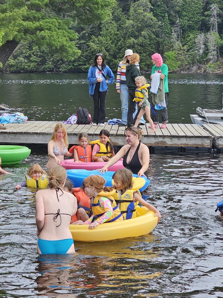 Children play with floaties beside a dock while adults stand by to supervise