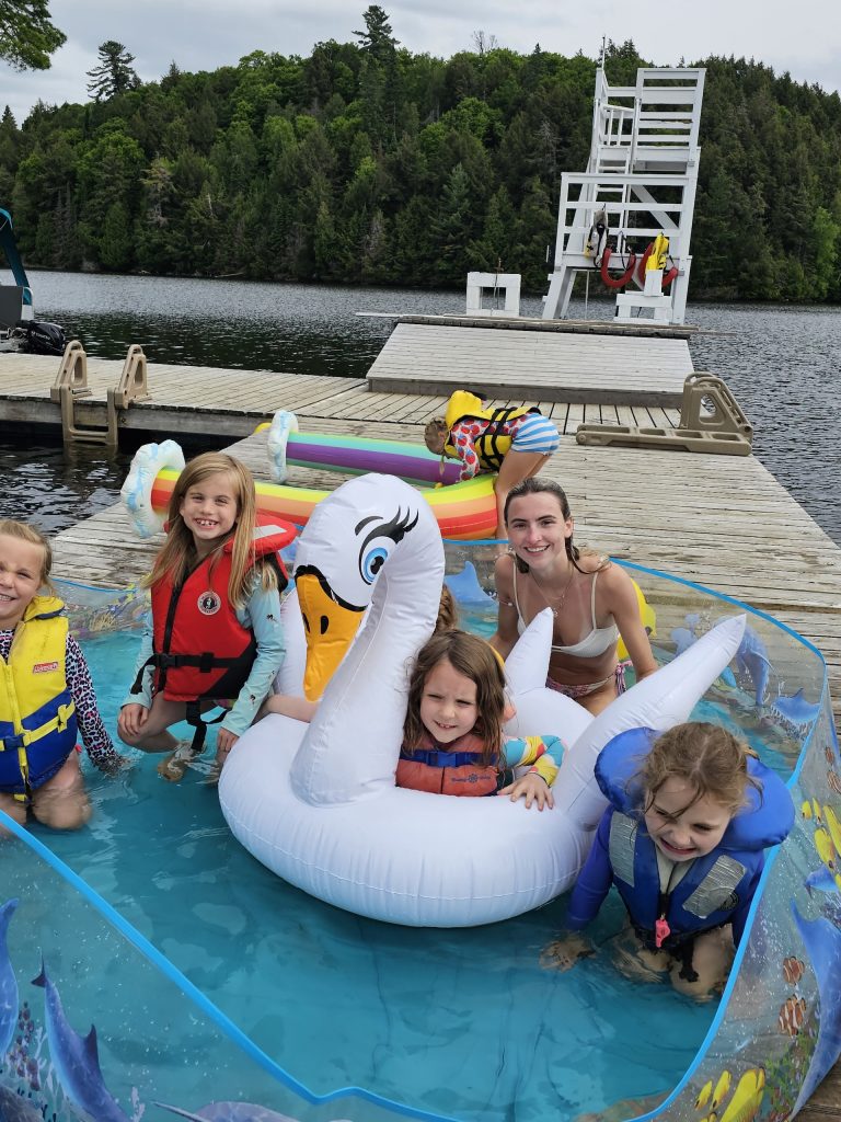 A group of smiling kids with a swan floatie on a dock