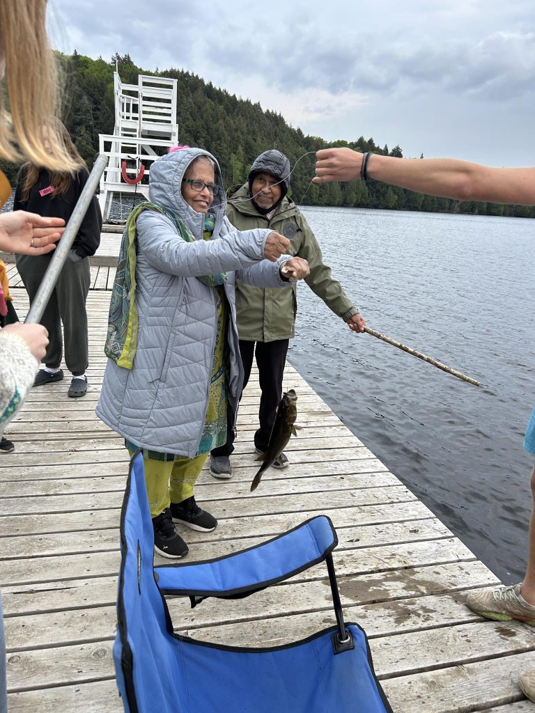 Several people stand on a dock; one in a grey padded coat has a fish on a line