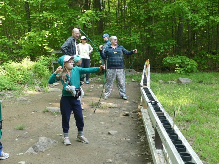 A row of people practicing archery, with a girl who has just loosed an arrow in the foreground