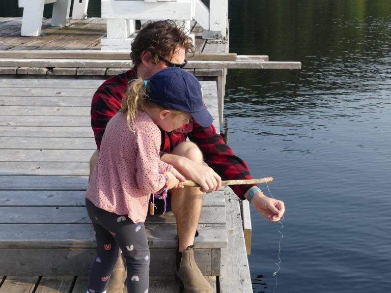 A man helps a young child fish from a dock