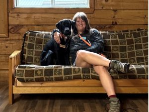 A woman relaxes on a couch with a dog sitting next to her