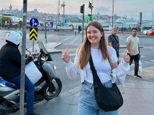 A woman stands smiling in front of a street sign