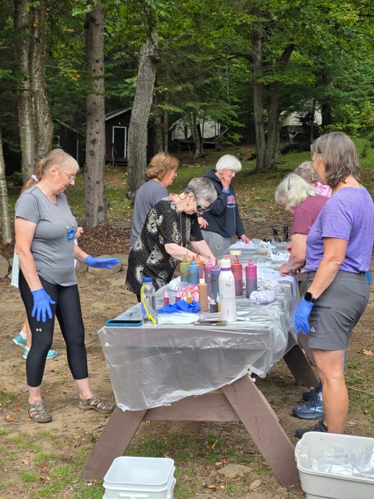 A group of people gather around a picnic table covered in bottles of paint