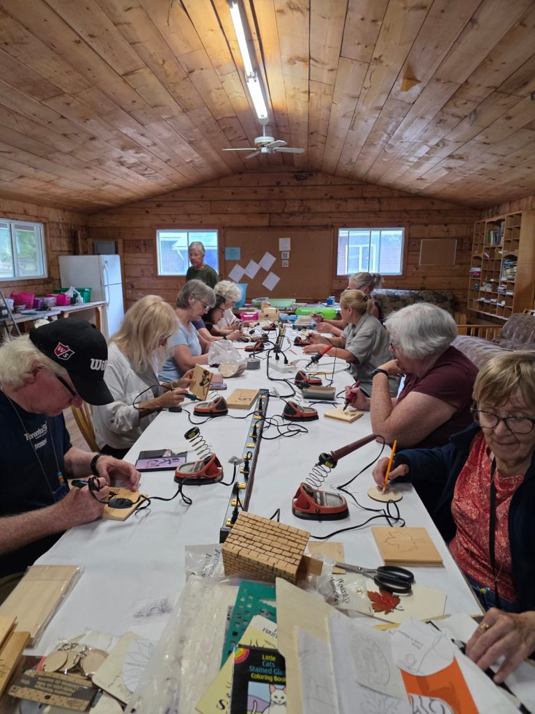 A long table, with people seated doing wood-burning art