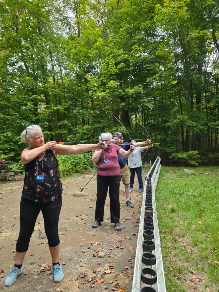 Four people stand at an archery range aiming their bows
