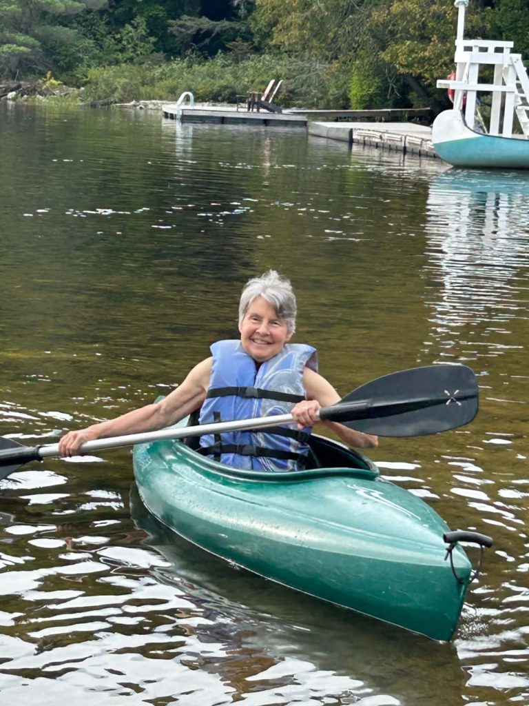 A woman in blue life jacket paddles a green kayak