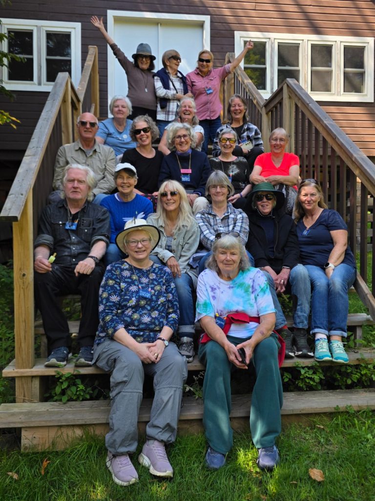 A group of older adults sits on the sets of a cabin posing for a group photo