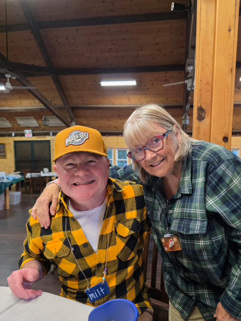 A man in an orange hat and a woman with red glasses pose for a photo