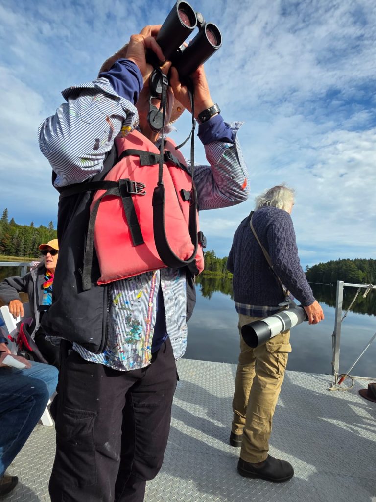 A man raises binoculars and looks into the distance while standing on a pontoon boat